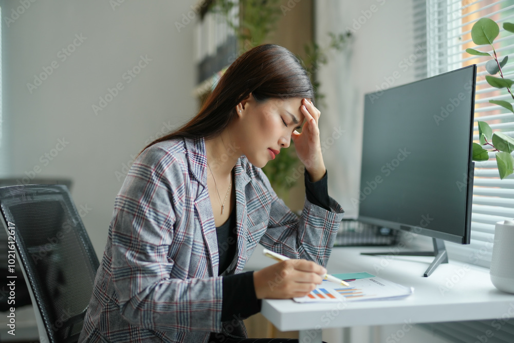 Young businesswoman is feeling tired and having a headache while sitting at her desk and analyzing financial charts Young businesswoman is feeling tired and having a headache while sitting at her desk and analyzing financial charts