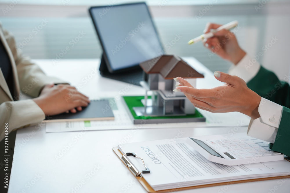 Real estate agent gesturing while showing a house model to client during meeting about purchase offer contract Real estate agent gesturing while showing a house model to client during meeting about purchase offer contract