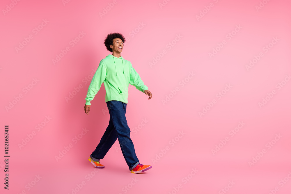 Full size photo of nice young man walk look empty space wear green hoodie isolated on pink color background Full size photo of nice young man walk look empty space wear green hoodie isolated on pink color background