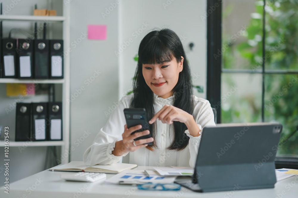 Asian accountant is using a smartphone to check financial data and analyze business growth while working in a modern office Asian accountant is using a smartphone to check financial data and analyze business growth while working in a modern office