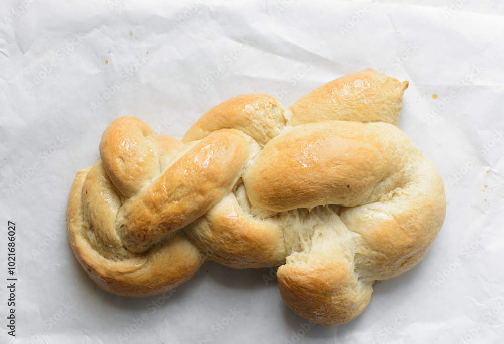 Overhead view of freshly baked challah on white parchment paper, top view of homemade braided challah, homemade challah baking fail Overhead view of freshly baked challah on white parchment paper, top view of homemade braided challah, homemade challah baking fail