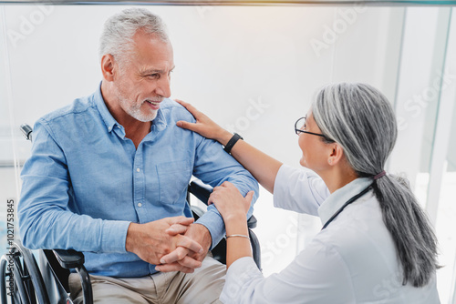 Smiling woman doctor talking to an old man in wheelchair taking care of him and support indoors