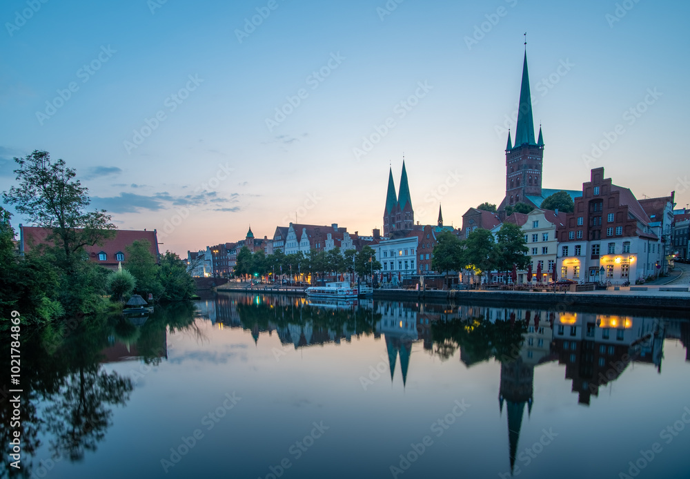 Obraz premium Silhouette der Altstadt von Lübeck, die sich in Fluss Trave spiegelt, vor Sonnenaufgang am Morgen