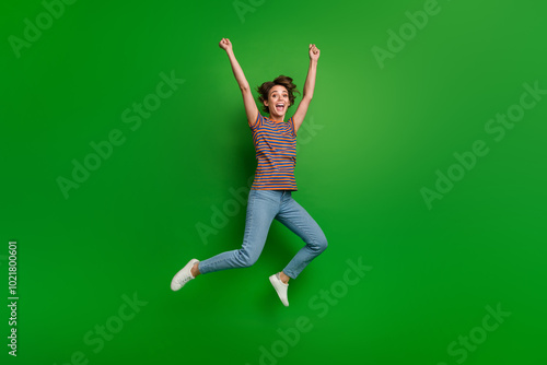 Full length portrait of delighted carefree person jumping raise fists achievement empty space isolated on green color background