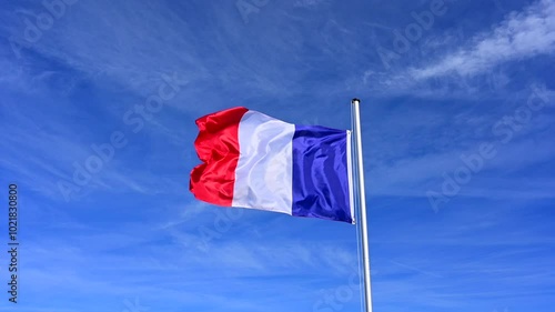 slow motion in strong wind, the flag of France is hoisted, flutters in the wind against a blue sky