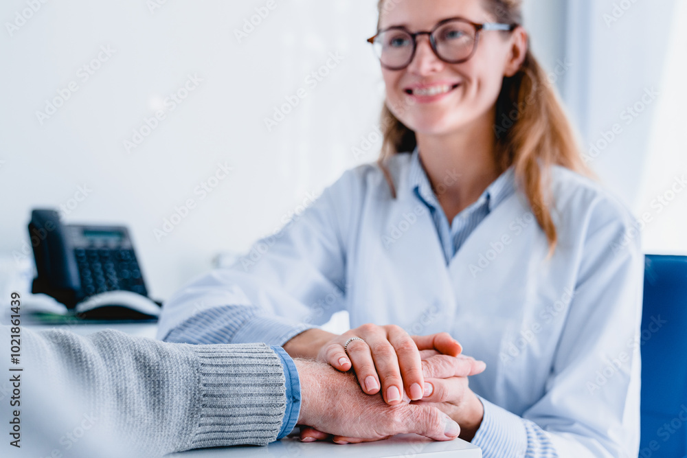 Smiling woman doctor in glasses holding her patient`s hand to support him Smiling woman doctor in glasses holding her patient`s hand to support him