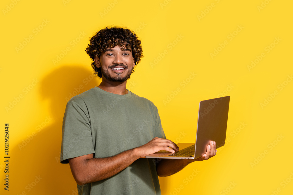 Photo of clever guy with wavy hairstyle dressed khaki t-shirt holding laptop in hands chatting isolated on yellow color background Photo of clever guy with wavy hairstyle dressed khaki t-shirt holding laptop in hands chatting isolated on yellow color background