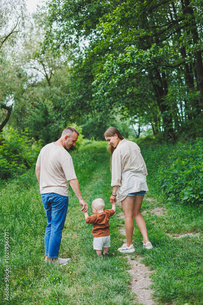 Obraz premium A family couple with a small son are standing in the park on the grass. Mother, father and child walk. Happy family with a child.