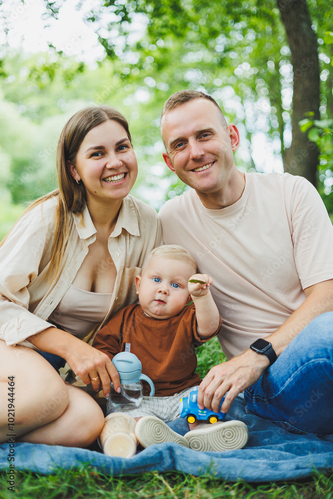 A family of a mother and father with a child in their arms, sitting in the park in the summer. The concept of a happy family with a small child, care and love. Happy family with a child. A family of a mother and father with a child in their arms, sitting in the park in the summer. The concept of a happy family with a small child, care and love. Happy family with a child.