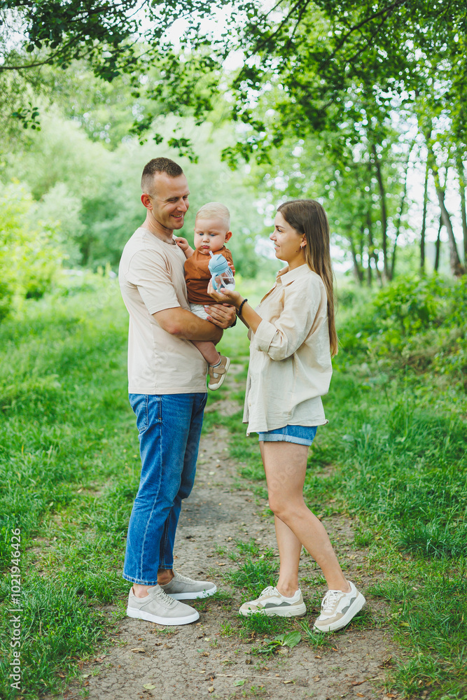 Fototapeta premium Mom, dad and little son on a walk in the park. Concept of parent time with child. Happy family couple with child in nature.