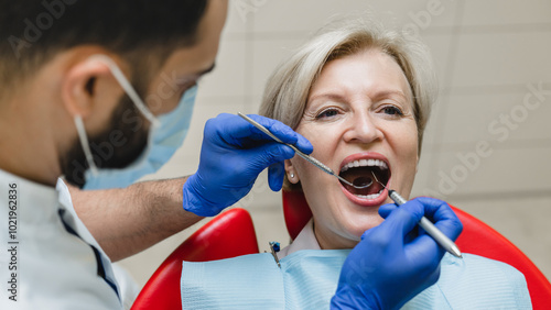 Opened mouth during stomatology checkup. Male dentist orthodont stomatologist curing operating filling tooth teeth mouth cavity to female patient. photo