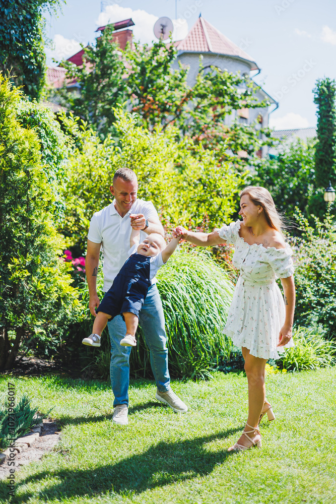 Fototapeta premium Two parents are playing on a walk with their toddler son. A young married couple, a man, a woman and a little son, are walking in the park. Time for a walk, mom, dad and small child.