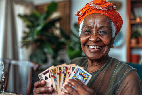 Happy elderly African-American senior woman looks into camera smiles with playing cards in her hands nurcery room. Activities and entertainment for pensioners photo