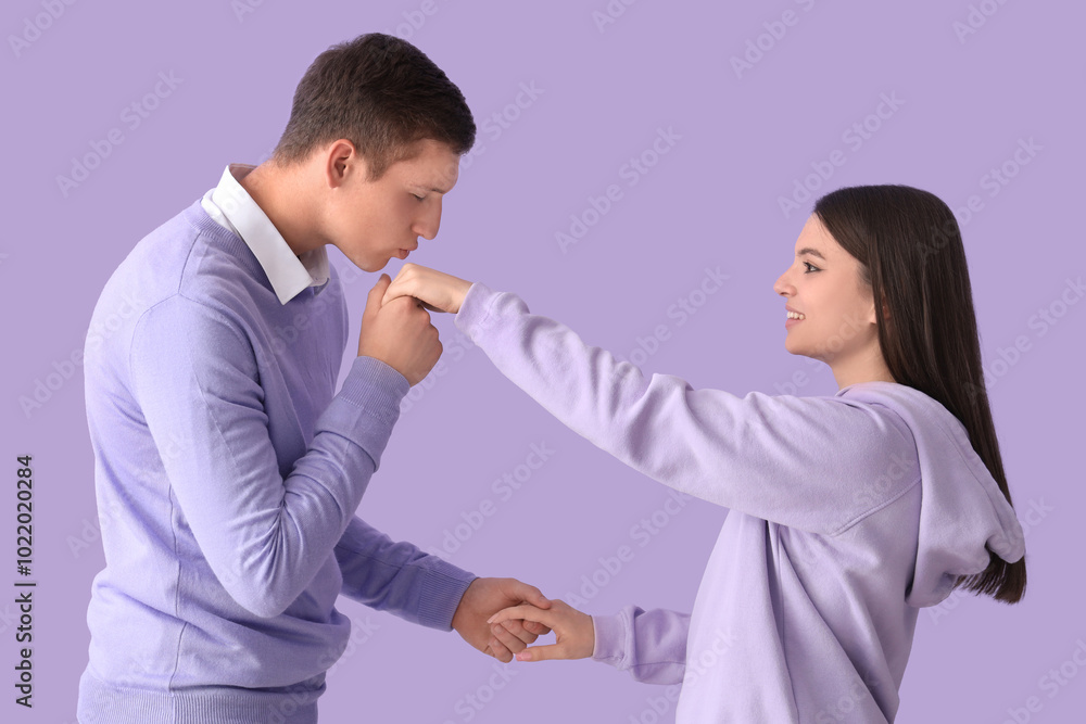 Young man kissing his girlfriend's hand on lilac background Young man kissing his girlfriend's hand on lilac background