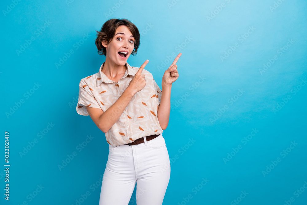 Portrait of astonished pretty lady indicate fingers empty space information isolated on blue color background Portrait of astonished pretty lady indicate fingers empty space information isolated on blue color background