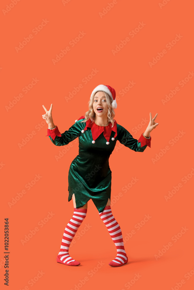 Happy young woman dressed as elf showing victory gesture on orange background Happy young woman dressed as elf showing victory gesture on orange background