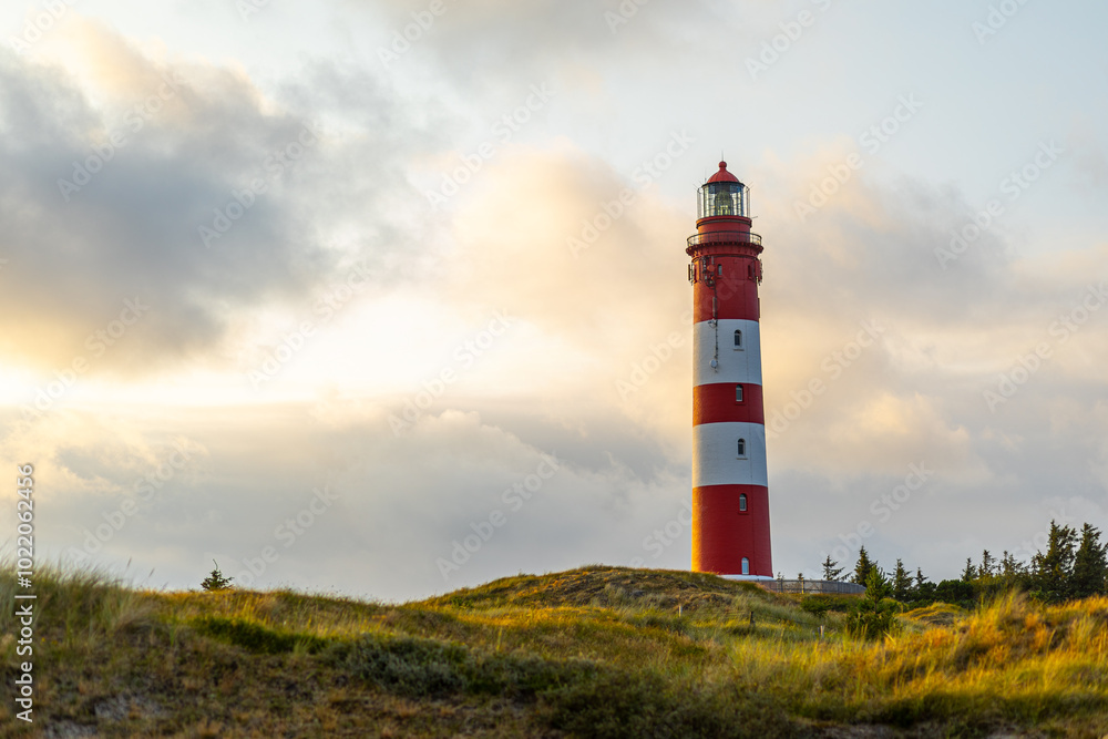 A striking red and white lighthouse stands tall against a colorful sunset sky, surrounded by rolling hills and lush greenery A striking red and white lighthouse stands tall against a colorful sunset sky, surrounded by rolling hills and lush greenery