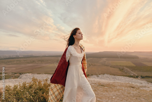 Woman in white dress standing on top of a hill with sunset in background, travel beauty nature fashion concept