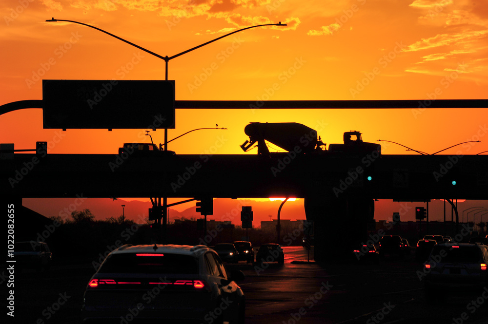 Bright yellow-orange sunset light silhouettes the vehicular traffic on a hot summer day at the Loop 202 underpass at Elliot Road in Mesa, Arizona