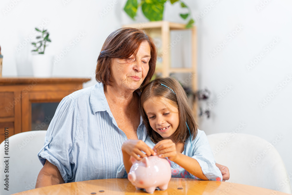 Φωτογραφία Happy granddaughter inserting coin in piggy bank while sitting with grandmother at home