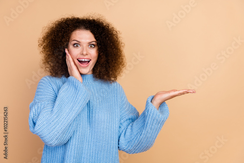 Photo of young saleswoman promoting surprisingly cheap deal holding hand touching cheek amazed isolated on beige color background photo