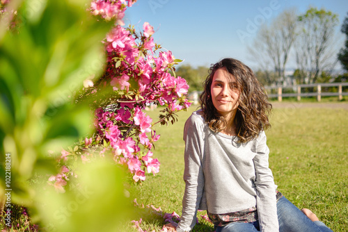 young woman sitting on lawn, next to pink flowers, on a sunny day