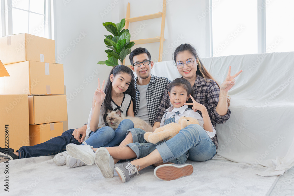 Happy Asian family with two children and cat sitting on couch in new home, surrounded by moving boxes. Parents and kids making peace signs. cardboard boxes, playfully unpacking. Relocation concept. Happy Asian family with two children and cat sitting on couch in new home, surrounded by moving boxes. Parents and kids making peace signs. cardboard boxes, playfully unpacking. Relocation concept.