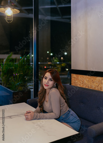 Beautiful brunette young asian woman sitting alone and relax inside cafe looking at camera.