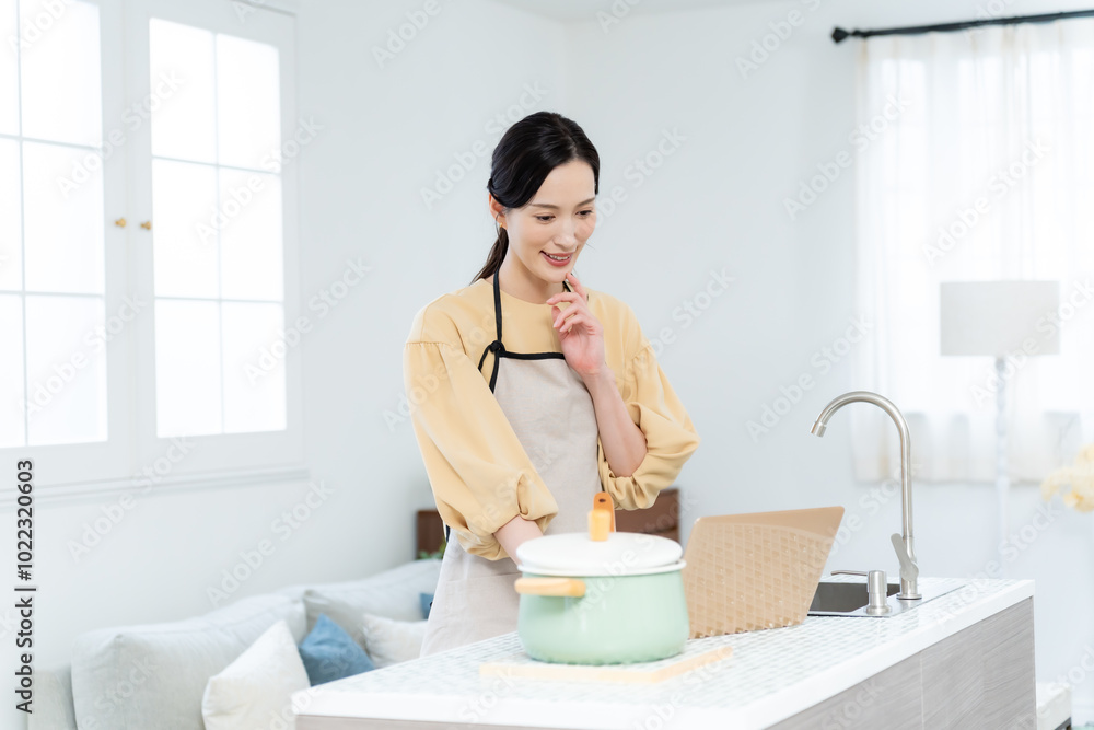 キッチンでパソコンを見ながら料理をする女性 キッチンでパソコンを見ながら料理をする女性