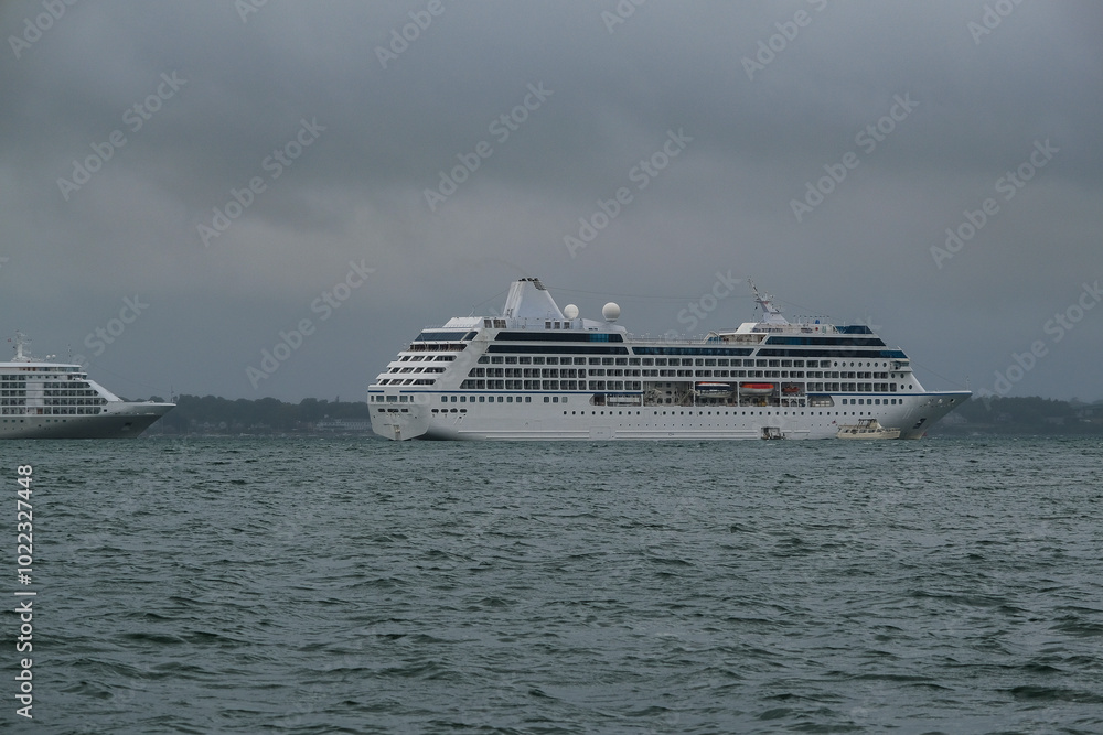 Small luxury cruiseship cruise ship liner Nautica anchoring at sea in bay of Newport, Rhode Island on grey cloudy day with swell, bridge and tender boats Small luxury cruiseship cruise ship liner Nautica anchoring at sea in bay of Newport, Rhode Island on grey cloudy day with swell, bridge and tender boats
