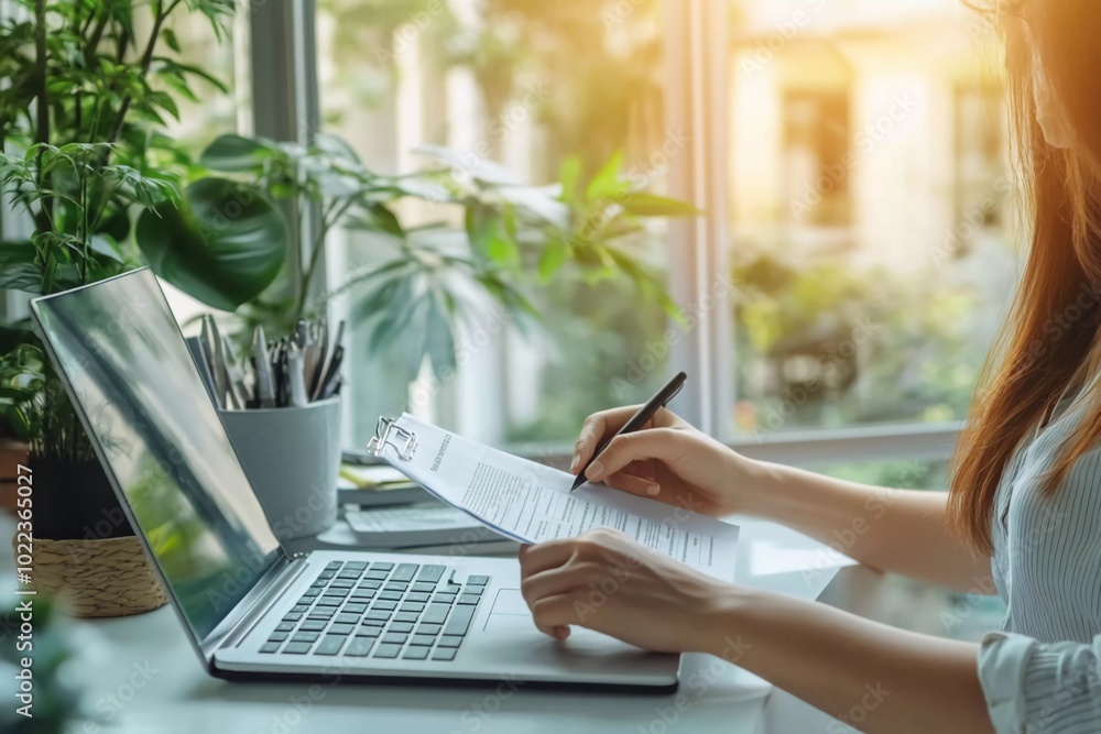 A business woman is working with a laptop computer and using a calculator to complete an online form on a white desk in the office A business woman is working with a laptop computer and using a calculator to complete an online form on a white desk in the office