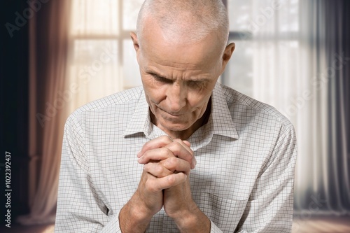 Nervous worried old man praying at home.