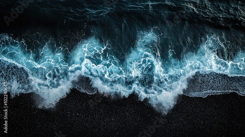 Fototapeta Naklejka Na Ścianę i Meble -  a teal and blue sapphire wave crashes onto a dark, black sandy beach, captured from a bird's eye view. The wave is moving upwards. The bottom