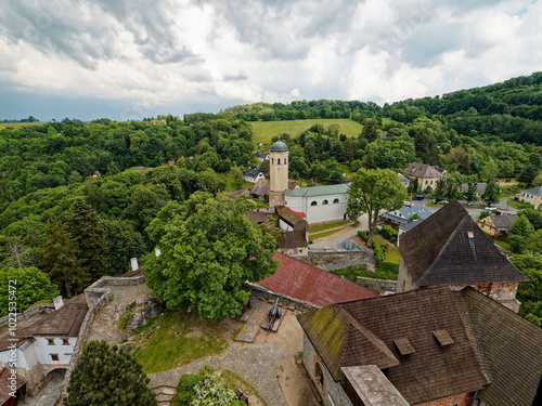 The view from Sovinec Castle in the Bruntál region shows lush greenery, rolling hills, and a quaint village below. This is the largest castle complex in the area and one of the largest in Moravia.