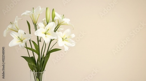 A bouquet of white lilies in a glass vase on a light brown background.