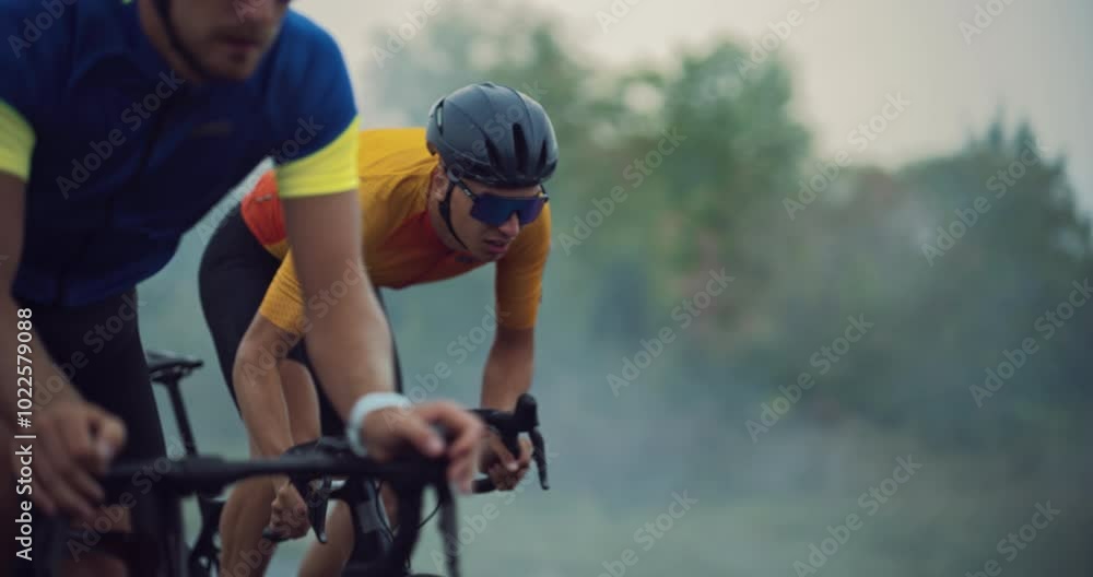 With Determined Expression Athlete Overtakes the Leader of the Pack During a Bicycle Race. Three Cyclists Ride Along the Road, Bikes Cutting Through the Wind on a Cloudy Day With Determined Expression Athlete Overtakes the Leader of the Pack During a Bicycle Race. Three Cyclists Ride Along the Road, Bikes Cutting Through the Wind on a Cloudy Day