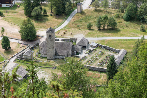 Old stone mountain church with bell tower and small cemetery, view from above. Macugnaga, Italy. On the left you can see the old Lime tree, a monumental tree from the 13th century photo