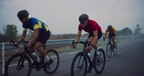 Cyclist Team of Three Men Rides Along the Open Road, Cloudy Sky Above Matching the Serious Mood of Their High-Intensity Practice. Riders Work in Tandem, Switching Leaders to Preserve Energy