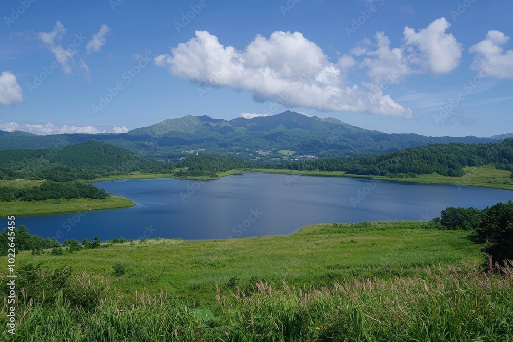 Serene lake surrounded by lush green hills and majestic mountains under a bright blue sky Serene lake surrounded by lush green hills and majestic mountains under a bright blue sky