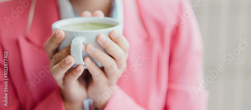 Close-up of a woman in a pink blazer holding a cup of green tea, creating a warm and cozy atmosphere.