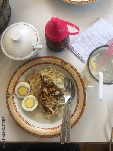 Traditional Cirebon noodle dish, 'Mie Koclok, served with tender shredded chicken, boiled egg halves, and fried onions in a creamy, rich coconut milk broth photo