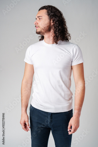 A young man stands confidently in profile, wearing a plain white t-shirt and dark jeans against a neutral background