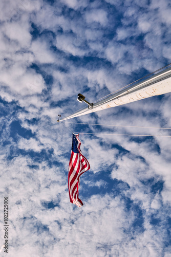 A United States flag elegantly flying on a mast against a picturesque sky filled with clouds, symbolizing patriotism and freedom under the bright daylight.