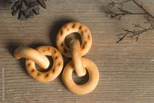 Ring shaped bagels, biscuits, cookies on wooden table with cones and dry tree branches emphasizing autumn season photo