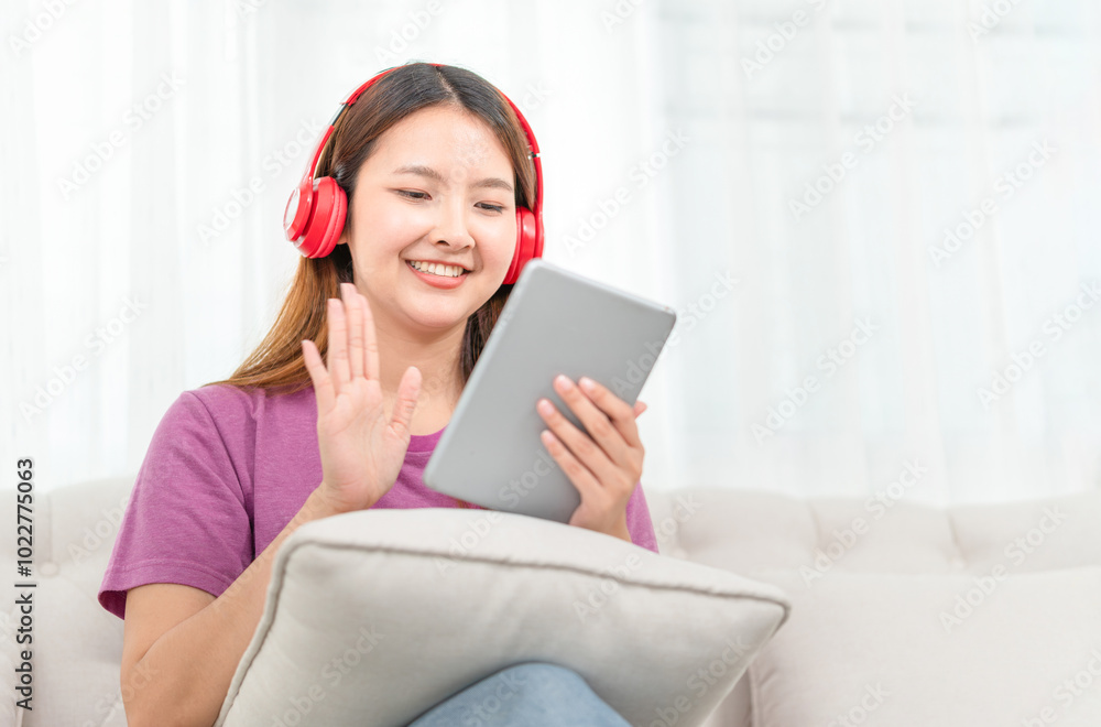 Relaxing casual young woman using a tablet PC having a video call, Asian woman listening to music with headphone from streaming online playing music Relaxing casual young woman using a tablet PC having a video call, Asian woman listening to music with headphone from streaming online playing music