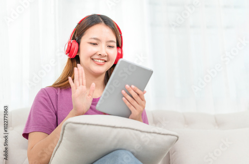 Relaxing casual young woman using a tablet PC having a video call, Asian woman listening to music with headphone from streaming online playing music