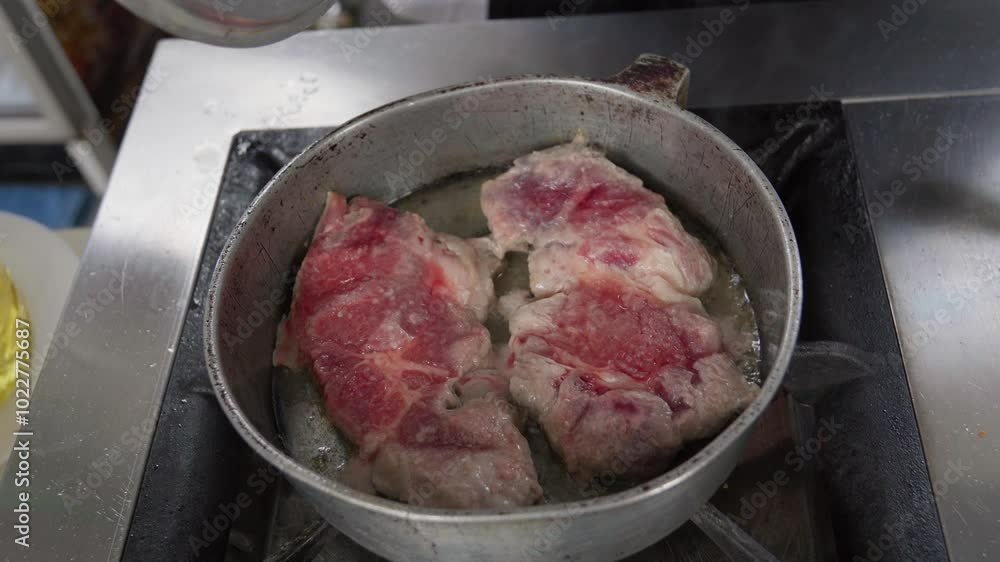 Chef frying two pieces of meat in pan on professional kitchen stove creates mouthwatering scene. Sizzling sound and aroma enhance culinary experience in restaurant Chef frying two pieces of meat in pan on professional kitchen stove creates mouthwatering scene. Sizzling sound and aroma enhance culinary experience in restaurant