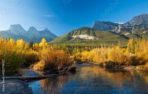 Beautiful scenery of the Canadian Rockies at dawn in autumn. Mountain, forest in yellow and green color reflected on water. Canmore, Alberta, Canada. The Three Sisters trio of peaks.