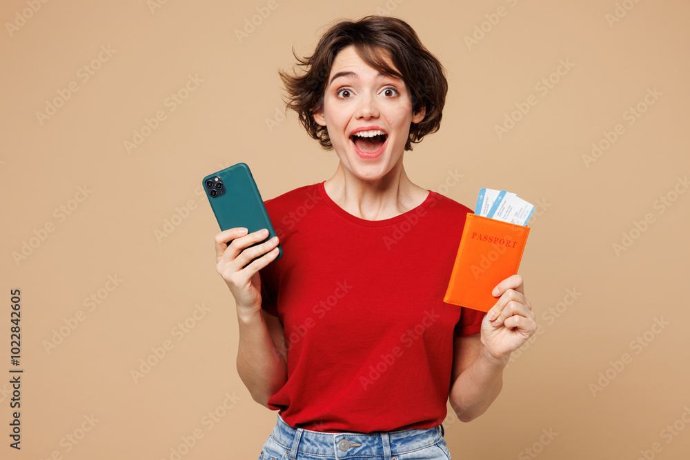 Traveler woman wear red casual clothes hold passport ticket mobile cell phone isolated on plain beige background. Tourist travel abroad in free spare time rest getaway Air flight trip journey concept