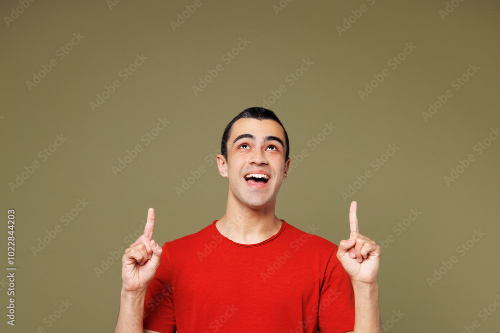Young happy surprised shocked middle eastern man he wears red t-shirt casual clothes point index finger overhead indicate on area isolated on plain pastel green background studio. Lifestyle concept. Young happy surprised shocked middle eastern man he wears red t-shirt casual clothes point index finger overhead indicate on area isolated on plain pastel green background studio. Lifestyle concept.